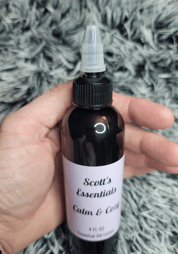 Hand holding a bottle labeled 'Scott's Essentials Calm & Cozy' with lid open