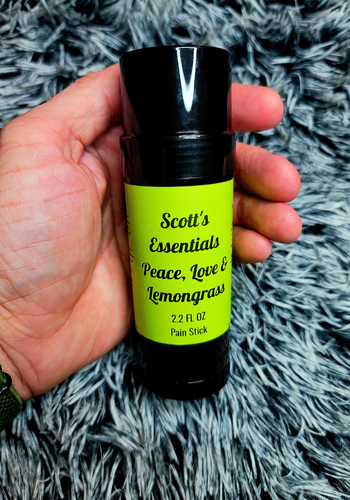 Hand holding a bottle labeled 'Scott's Essentials Peace, Love & Lemongrass' on a gray textured background