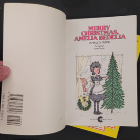 Book open to a page with a Christmas illustration of Amelia Bedelia, featuring a tree.