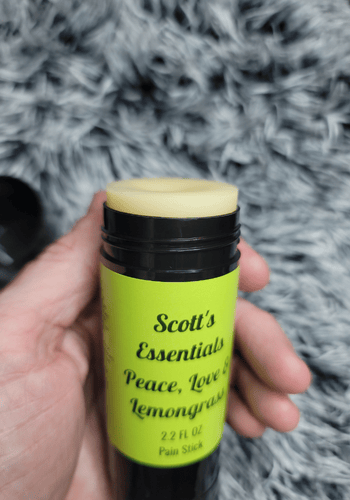 Hand holding a lemongrass pain stick labeled 'Scott's Essentials' against a gray textured background