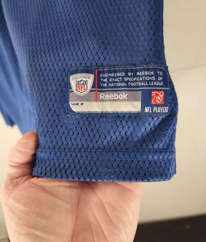 Blue sports jersey with Reebok and NFL logos on a beige background