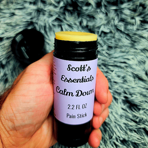 Hand holding a pain stick labeled 'Scott's Essentials Calm Down' against a textured green background
